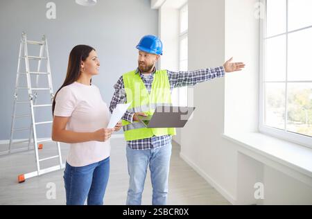 Young woman standing with foreman in new empty apartment discussing design project or repair Stock Photo