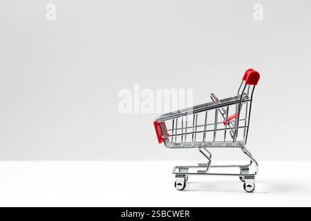 Side view closeup of shiny aluminum empty miniature shopping supermarket cart with red handle isolated on white background Stock Photo