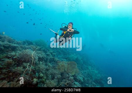 Scuba diver making heart hands swimming on tropical coral reef Stock Photo