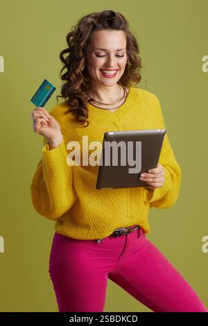 happy fit woman on green background in yellow sweater with credit card using tablet PC. Stock Photo