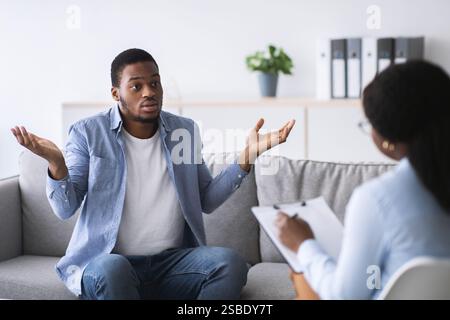 Puzzled young black guy having session with psychologist at mental health office Stock Photo