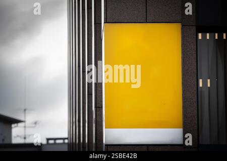 Selective blur on a A bright yellow sign hangs empty outside a modern storefront, awaiting custom branding. The bold, blank panel contrasts with the b Stock Photo