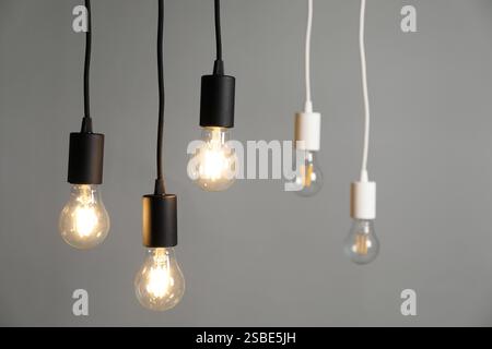 Light bulbs hanging on cords against grey background, selective focus Stock Photo