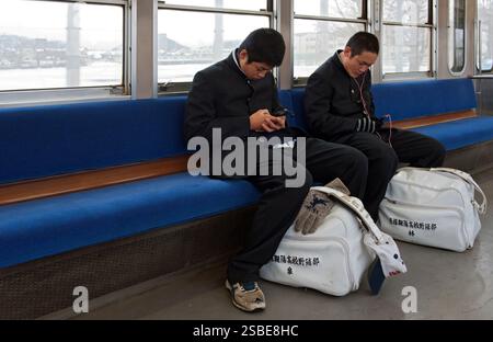 Two high school boys wearing matching traditional "gakuran" (black uniforms) looking at cell phones and carrying sports bags riding a train in Japan. Stock Photo