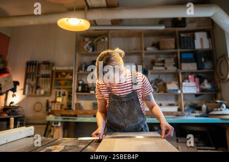 Woman carpenter inspecting wooden beam straightness with ruler before cutting with saw in workshop Stock Photo