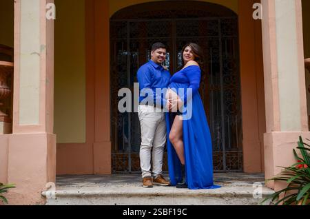 Happy pregnant couple posing in front of a building, touching belly and smiling Stock Photo