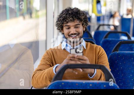 Public transport passenger uses phone while sitting. Man smiles contentedly typing message on smartphone and browsing social media. Stock Photo