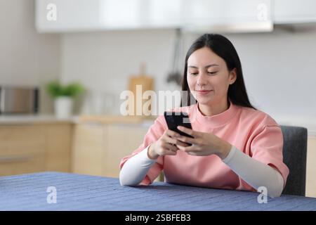 Satisfied asian woman using smart phone in the kitchen at home Stock Photo