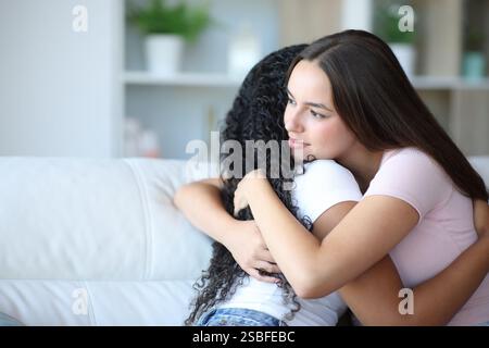 Satisfied woman hugging her friend sitting on a couch at home Stock Photo
