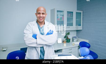 Smiling Dentist Standing Confidently in a Modern Dental Office with Crossed Arms and Professional Attire Stock Photo