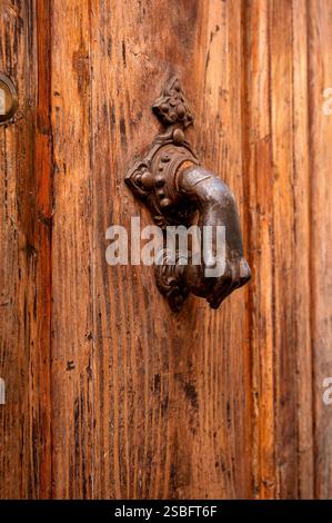 Antique metal hand-shaped door knocker on a weathered wooden door Stock Photo