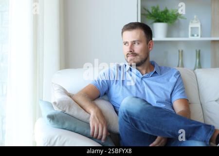 Proud man sitting on a couch looking through a window at home Stock Photo