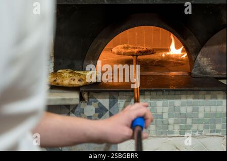 Baker taking focaccia bread from wood fired oven using a peel in a bakery Stock Photo