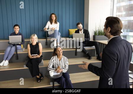 Male presenter makes speech standing in front of team Stock Photo