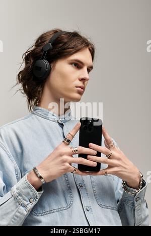 Handsome young man adorned in stylish jewelry listens to music while focused on his smartphone. Stock Photo