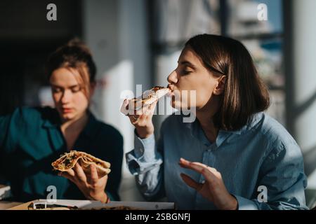 Two women enjoying pizza during a casual lunch break Stock Photo