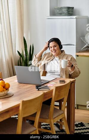 Smiling woman in casual attire relaxes with coffee while enjoying a virtual conversation. Stock Photo