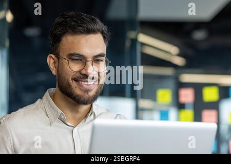 Successful businessman in shirt close up working with notebook inside office. Man smiling contentedly reviewing electronic report, joyful financier investor. Stock Photo