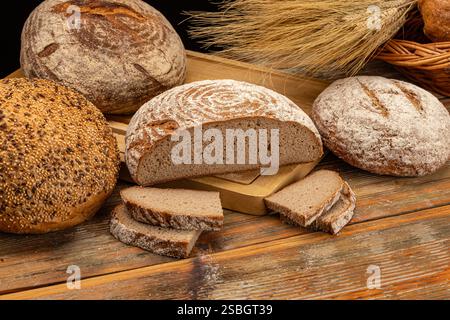 Different kinds of bread are presented on a wooden table with wheat ears, creating a rustic bakery atmosphere Stock Photo