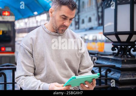 Focused Man Using Tablet While Waiting at Train Station Stock Photo
