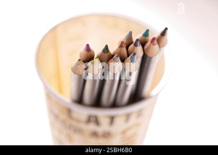 A set of colored pencils is shown lying in a cup, illuminated from behind. Stock Photo