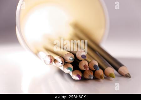 A set of colored pencils is shown lying in a cup, illuminated from behind. Stock Photo