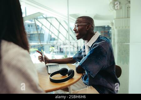 A male student sits in an urban college setting, actively conversing while working on a laptop, depicting modern education and communication. Stock Photo
