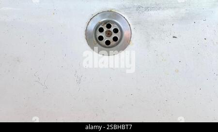 A small round drain on a worn white surface, showing dirt and age from use. Stock Photo