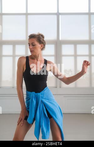 A woman performs a contemporary dance in a bright studio with large windows. Stock Photo