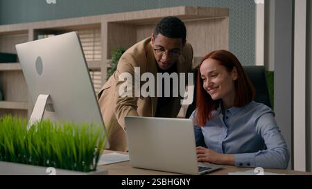 African American man boss mentor coach businessman teaching new employee at workplace team leader help advice Caucasian woman intern with laptop Stock Photo