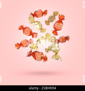 Candies in bright wrappers falling on pink background Stock Photo