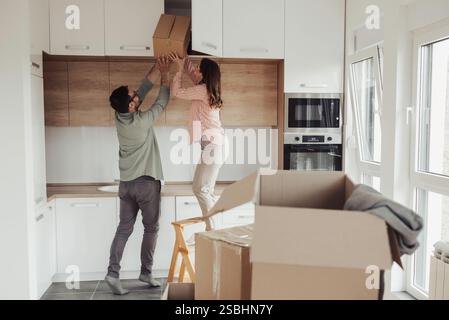 Young couple storing carton boxes in kitchen high elements, moving in concept and unpacking things Stock Photo