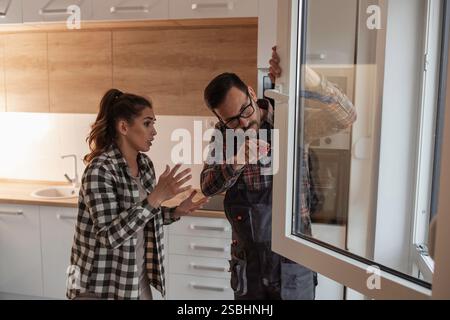 Repairman fixing window in apartment while young woman owner standing beside him Stock Photo