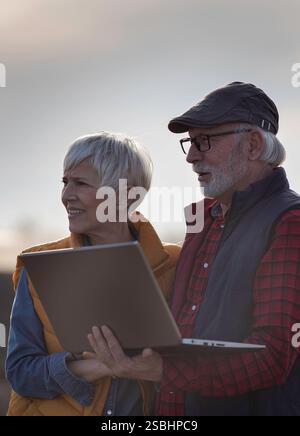 Mature farmers man and woman standing in field and looking at laptop Stock Photo