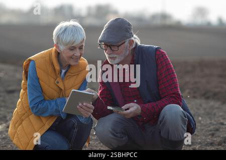 Senior farmer, man and woman checking soil quality and using tablet. Stock Photo