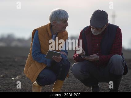 Senior farmers, man and woman checking soil quality and using tablet. Stock Photo