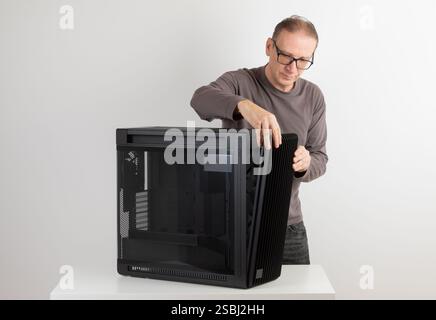 Man removing  15.5 mm front panel grille with 45% porosity with dust filter from  PC case, empty big tower, chassis, on side is tempered-glass. Stock Photo