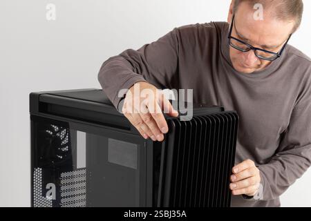 Man removing  15.5 mm front panel grille with 45% porosity with dust filter from  PC case, empty big tower, chassis, on side is tempered-glass. Stock Photo