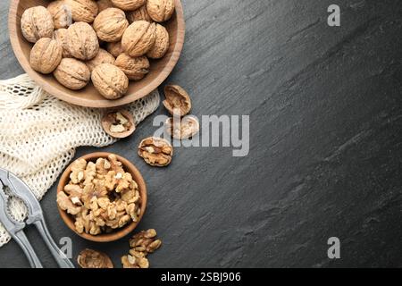 Fresh ripe walnuts, nutcracker and shells on black table, flat lay. Space for text Stock Photo