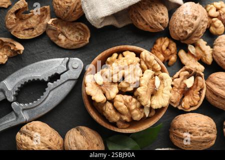 Fresh ripe walnuts, shells and nutcracker on black table, flat lay Stock Photo