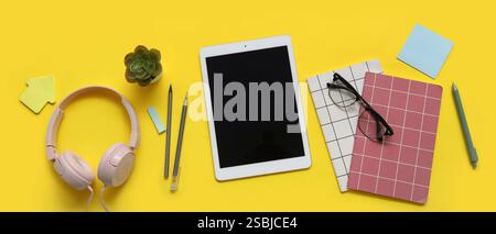 Tablet computer, headphones, eyeglasses and stationery on yellow background Stock Photo