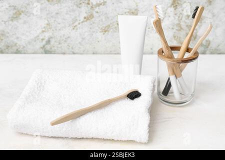 Holder with bamboo toothbrushes, paste and clean towel on light background Stock Photo
