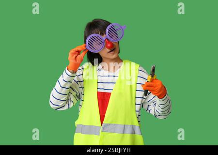 Funny young female builder with pliers on green background. Fool's day Stock Photo