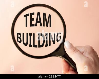 Team Building symbol. Concept word Team Building on magnifying glass. Businessman hand. Beautiful pink background. Business and Team Building concept. Stock Photo