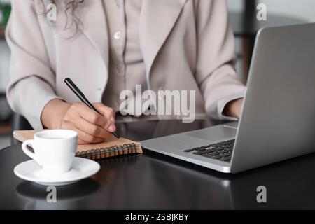 Female author with laptop taking notes at table in cafe, closeup Stock Photo
