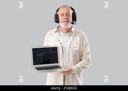 Mature programmer in headset with laptop on light background Stock Photo