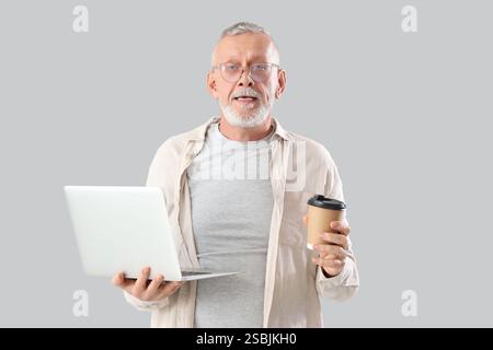 Mature programmer with laptop and coffee cup on light background Stock Photo