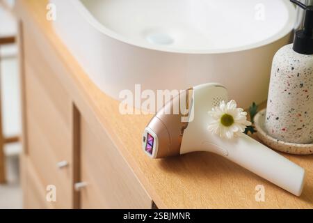 Modern photoepilator with flower on table near sink in bathroom Stock Photo
