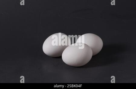 Three white chicken eggs on a dark background. Stock Photo