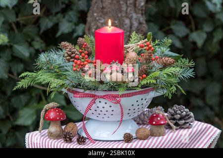 christmas arrangement with a red candle, coniferous branches, ilex berries, cones and walnuts in a vintage colander Stock Photo